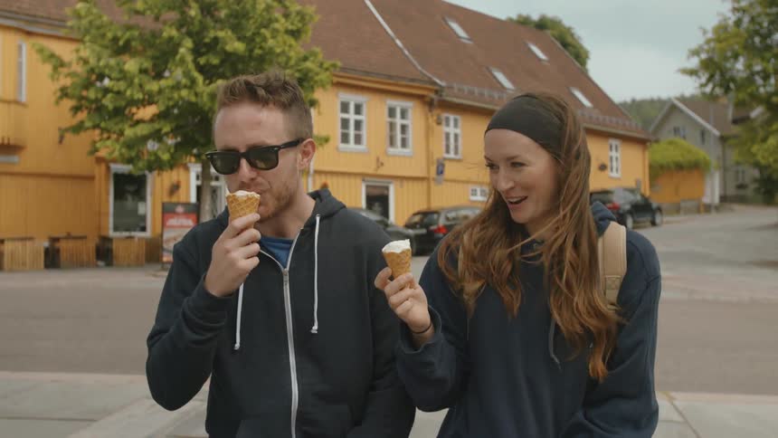 Man and woman smiling and talking while eating ice cream cones outside on windy day