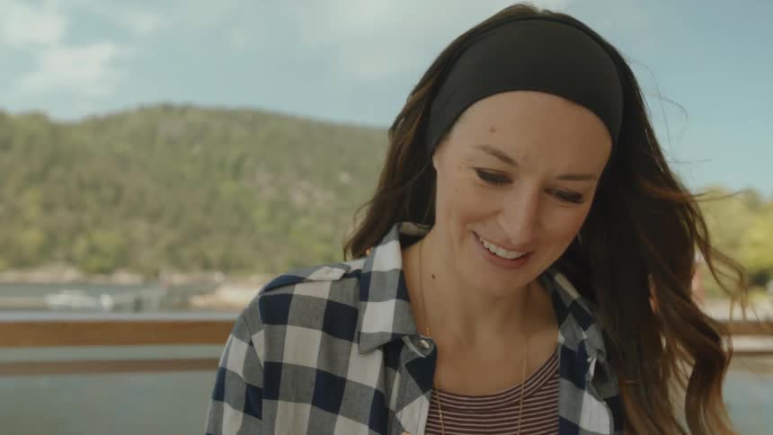 A woman is smiling as she looks down in a windy area