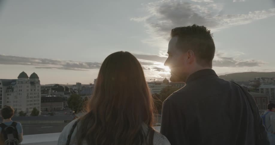 A man and woman overlook a city at sunset