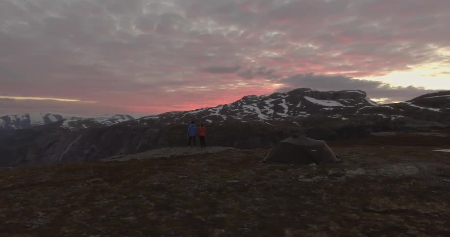 Two people are standing on the edge of a mountain top at sunset