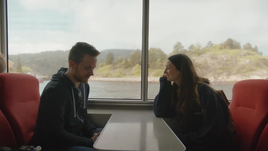 A man and woman talk while sitting at a table on a boat