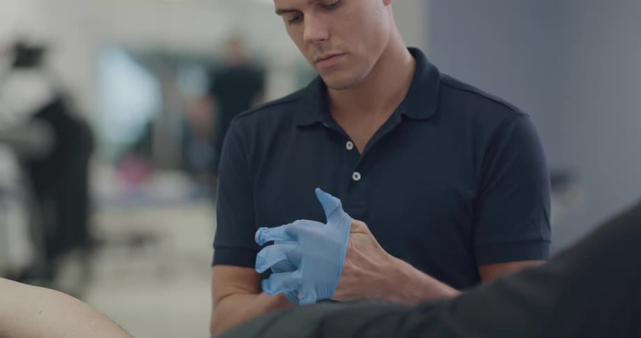 A physical therapist putting on latex gloves while a patient lies face down on a table
