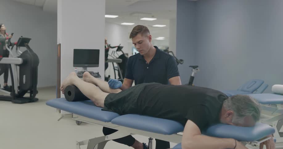 A man with gloves doing acupuncture to a man laying on a table in a gym