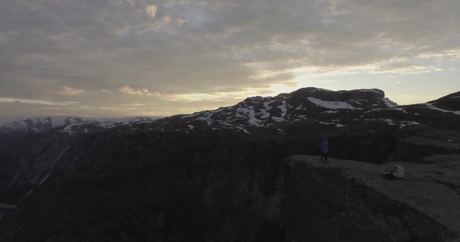 Two people are on the edge of a cliff at sunset