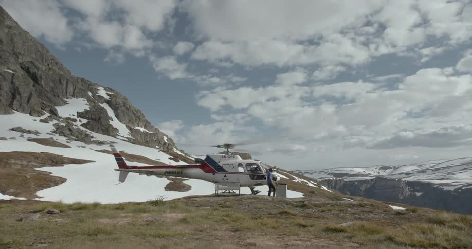 A man walks by a running helicopter on top of a mountain