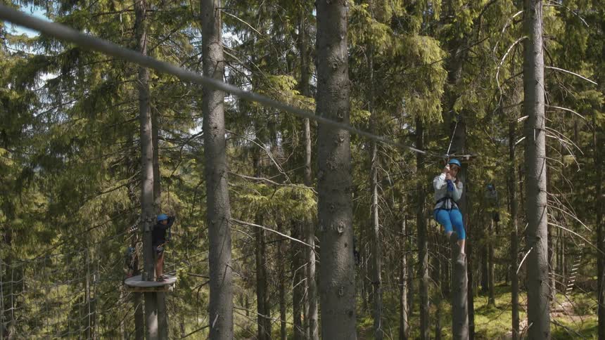 Woman riding down a zip line secured to tall trees