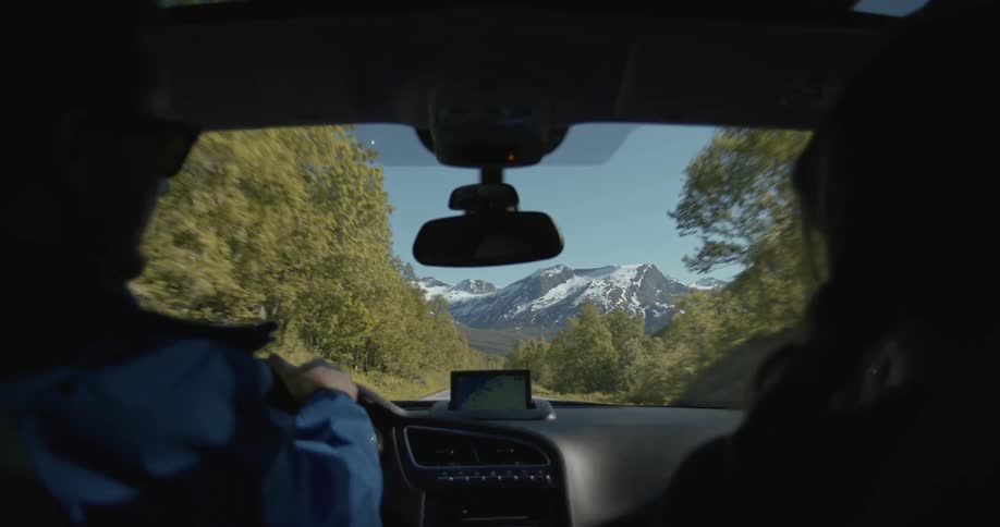 A man and woman in a car driving toward a mountain range