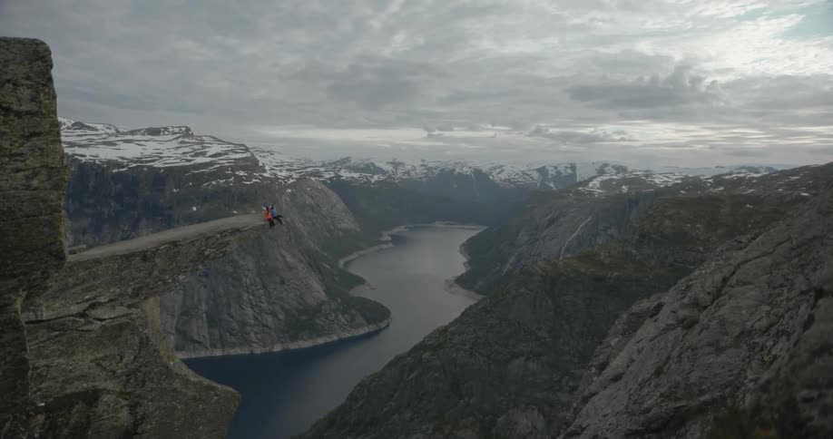 People sit on the edge of a cliff far above a mountain river