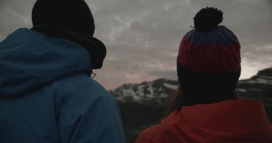 Two people wearing winter hats look towards a snow-capped mountain range