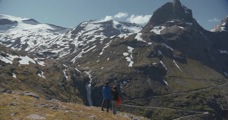 Man and woman standing and enjoying view of mountain with patches of snow