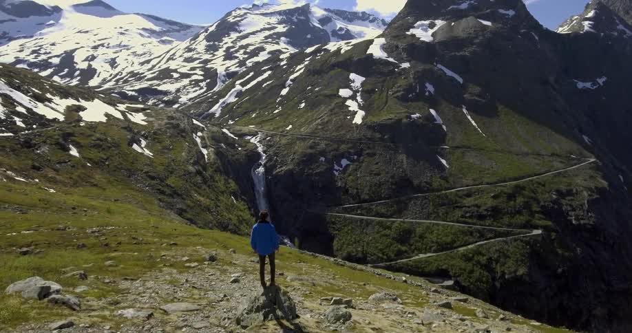 A person looking out over a grassy mountain and waterfall