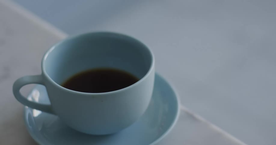 A blue ceramic cup filled with coffee over a blue ceramic plate over a table