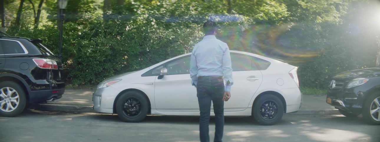 A man walks across a road to approach a parked car on a sunny day