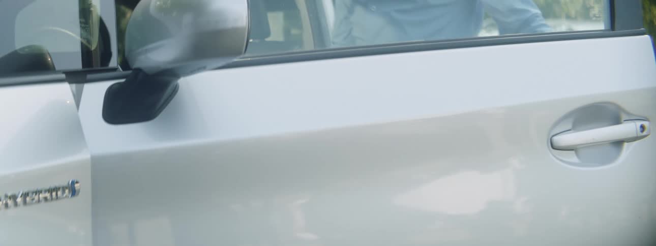 A man reaches out to grasp the door handle of a car to open it and enter the vehicle