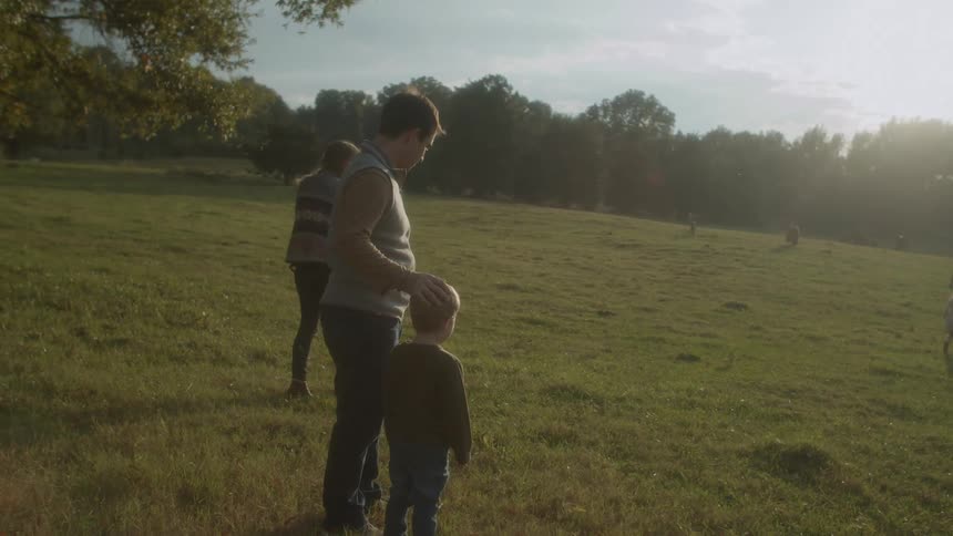 A family of a mother father and small children walk in a open grassy field with a cow