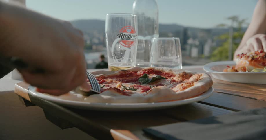 Utensils are used to cut pizza while a couple dines outside