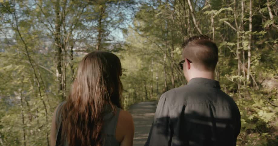 A man and woman walking down a trail in the woods on a sunny day