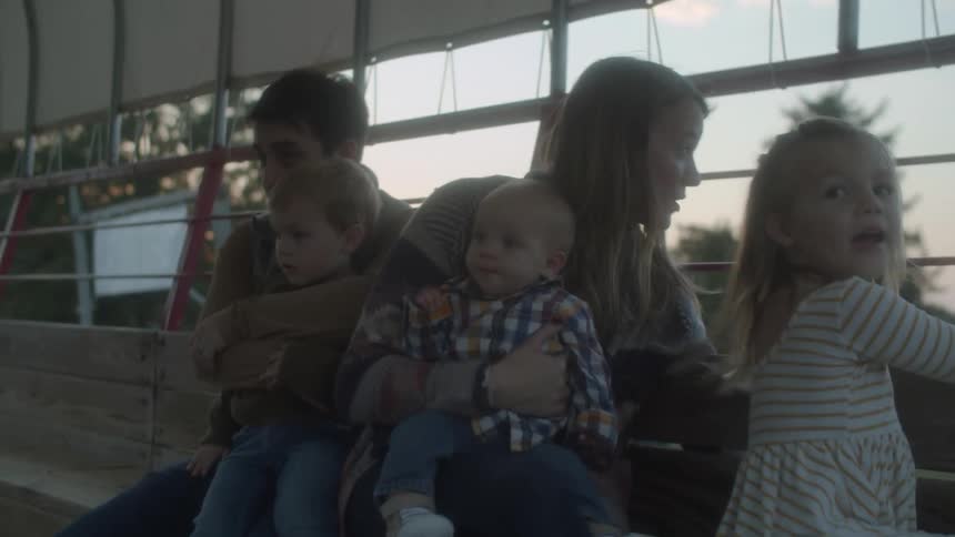 Mother and father each hold a younger child while daughter looks out at area public transport is passing