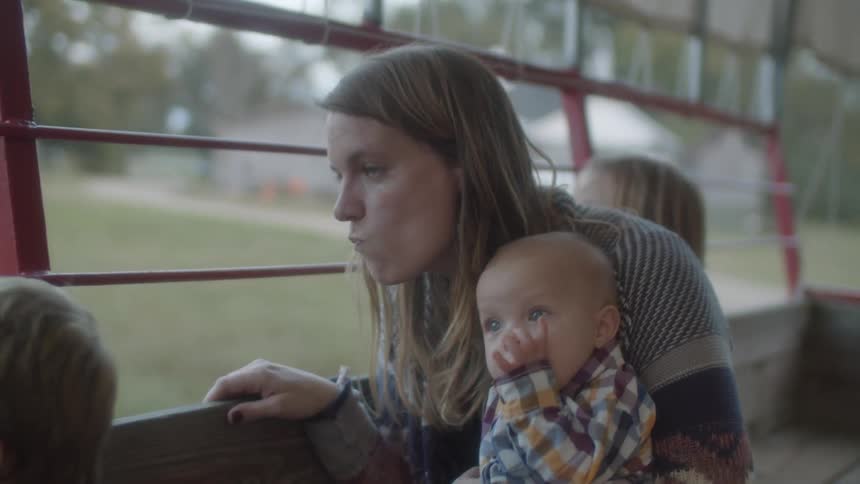 A woman with a baby on her lap talks to her son as she rides on the back of a trailer with her kids