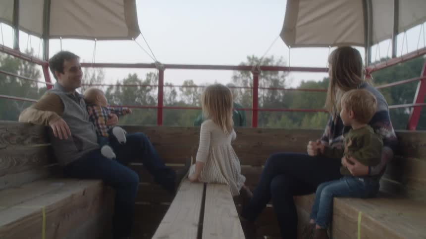 A family sits on wood benches in a moving vehicle that is covered with canvas