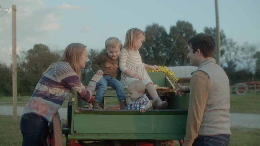 A mother and father stand next to a buggy that their three kids sit in