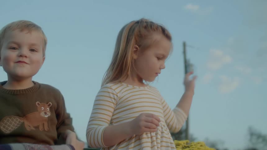 A boy and a girl sitting outdoors playing together at evening
