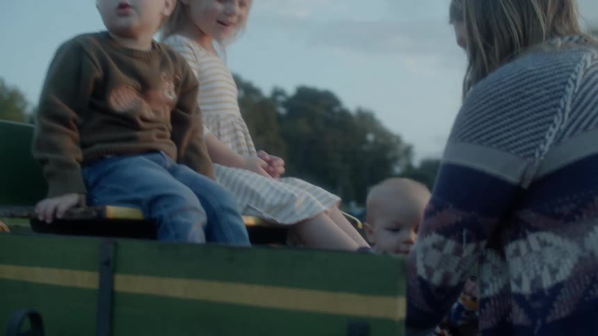 Mother puts a baby in a cart with his brothers for a picture at sunset