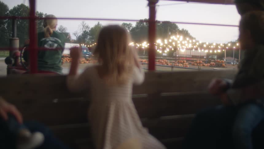 Young girl in a white dress riding a train around a pumpkin patch at evening