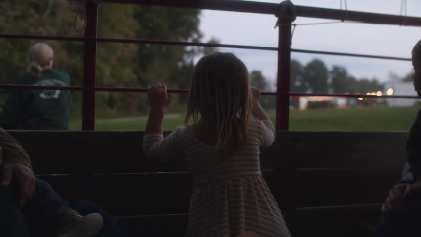 A small girl hangs onto and looks through a fence alongside another pair of children and their parents