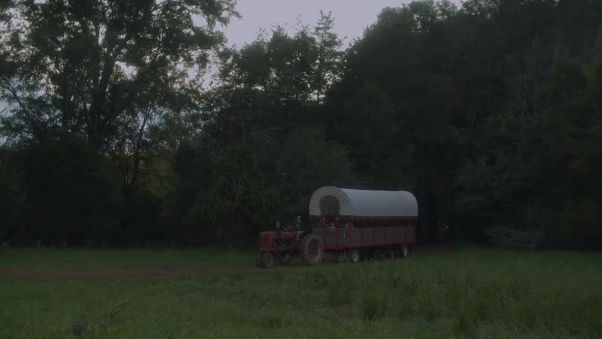 Tracker pulls covered wagon past trees in grassy area at night