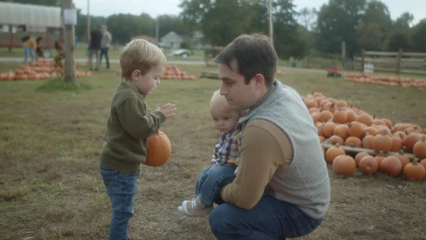 A father and two young sons outside at a pumpkin patch on an autumn day