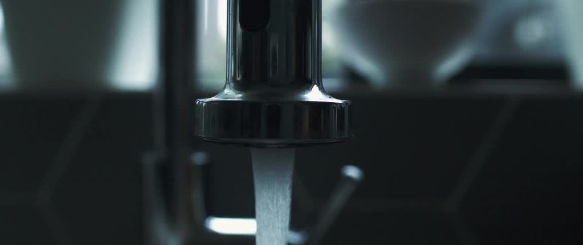A hand reaches out to turn the handle of a water faucet and water begins flowing out of it