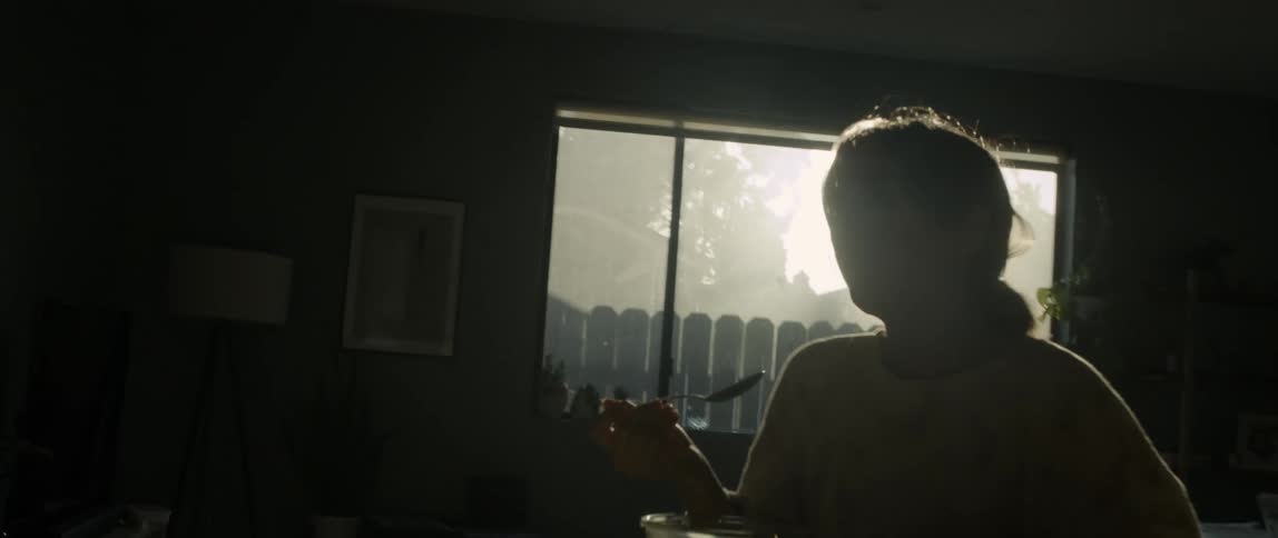 A woman sitting at a table eating with a wall and a window in the background