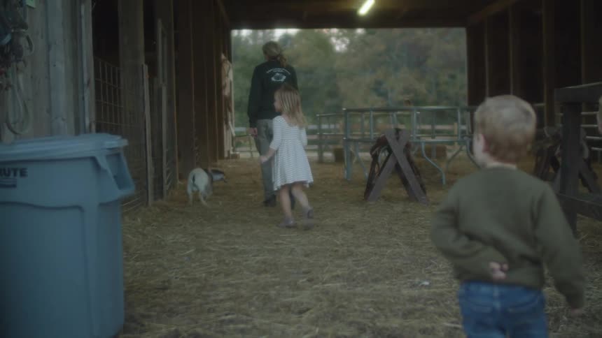 A man and a woman and children walking in a barn with goats