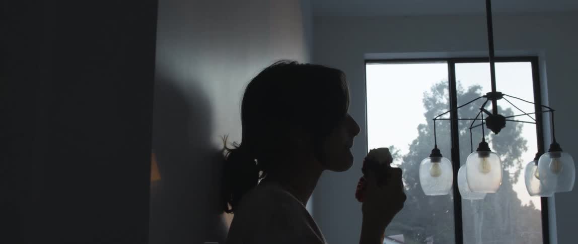 Woman leaning against wall eats near window showing trees