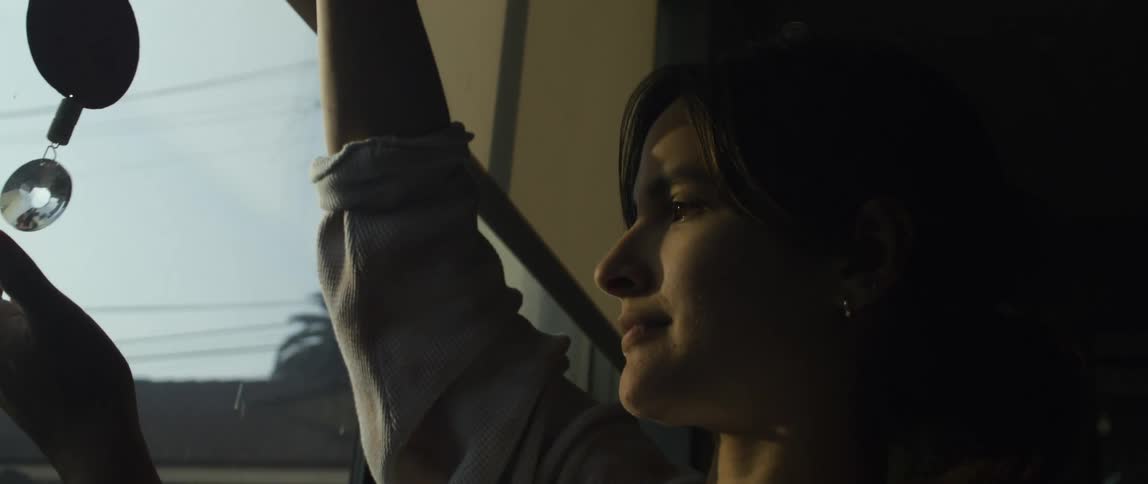 Woman near a window at home contemplates the light reflecting on a decorative pendant at sunset
