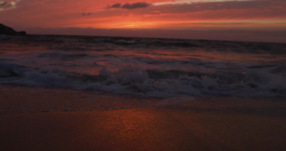 Waves crash on beach reflecting light tinting sky red