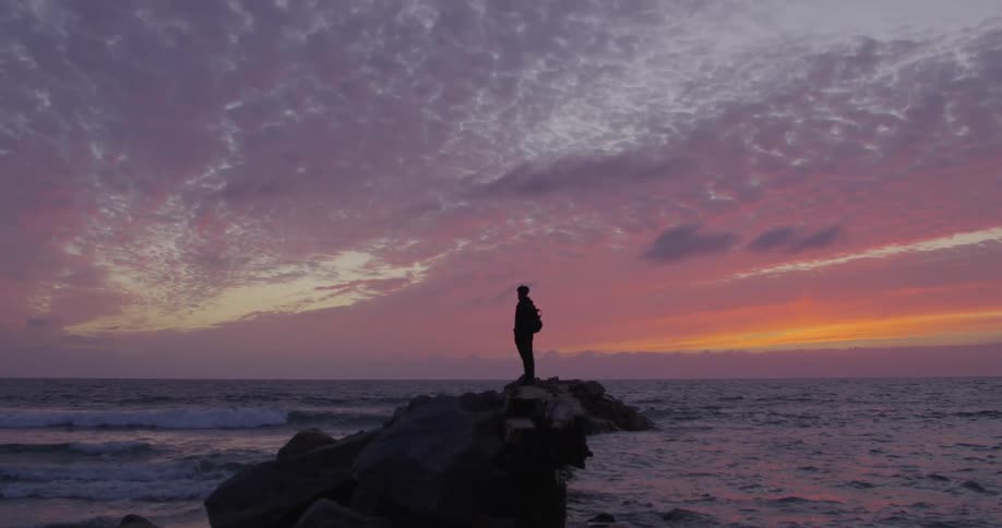 Silhouette of a man standing on a promontory on the ocean at sunset