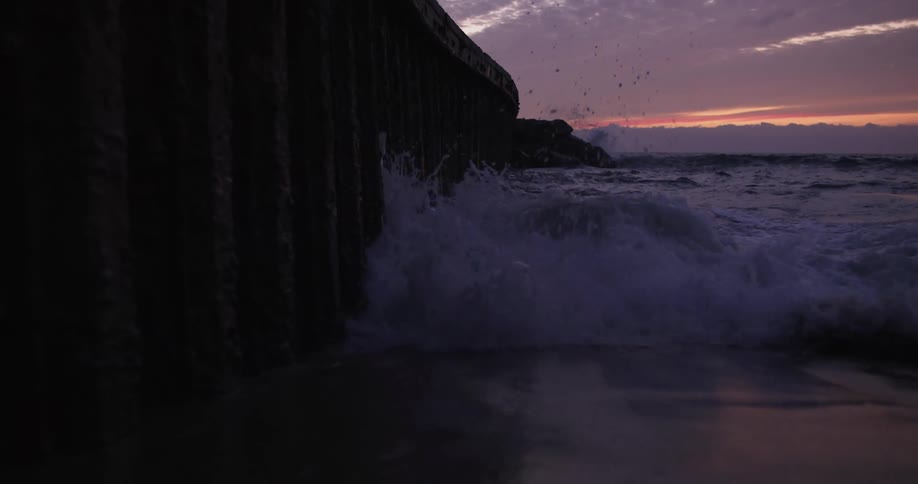 Fast moving waves crash onto a cliff and beach at dusk