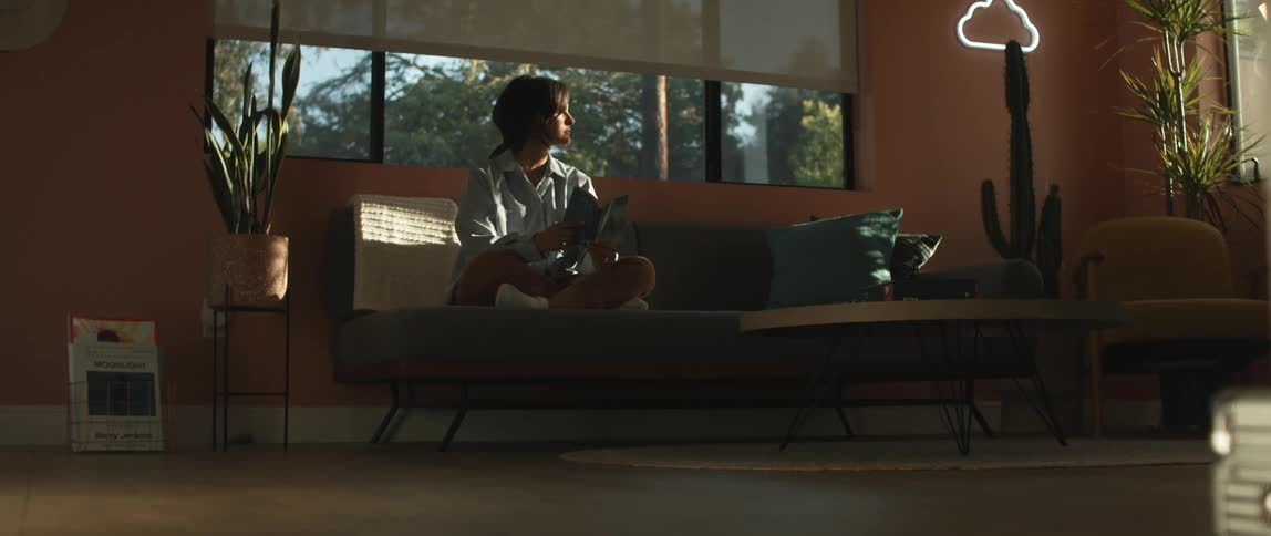 A woman sits alone on a living room couch reading a book