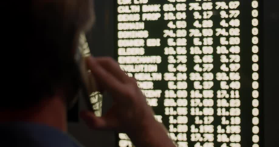 Man stands watching a screen with text and numbers talking on the phone