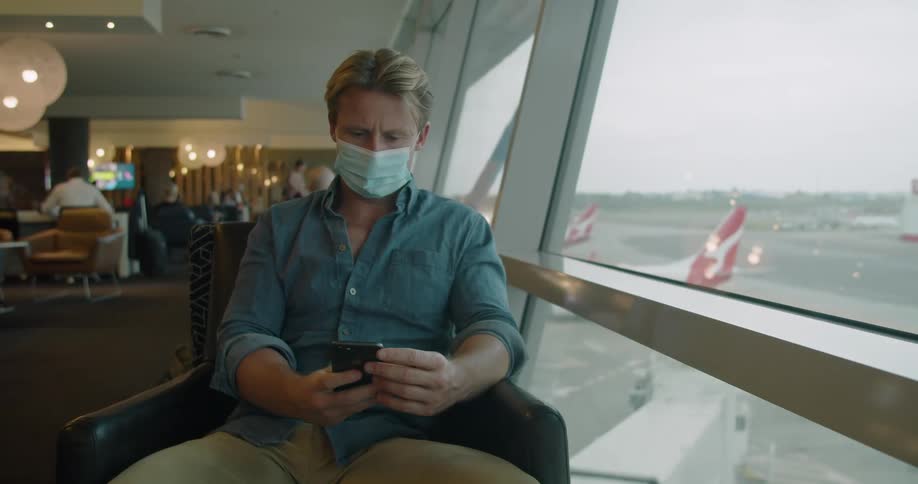 Man wearing a face mask sitting airport lounge making a call on a smartphone