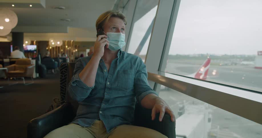 A man wearing a mask sitting on a chair talking on a smart phone in an airport