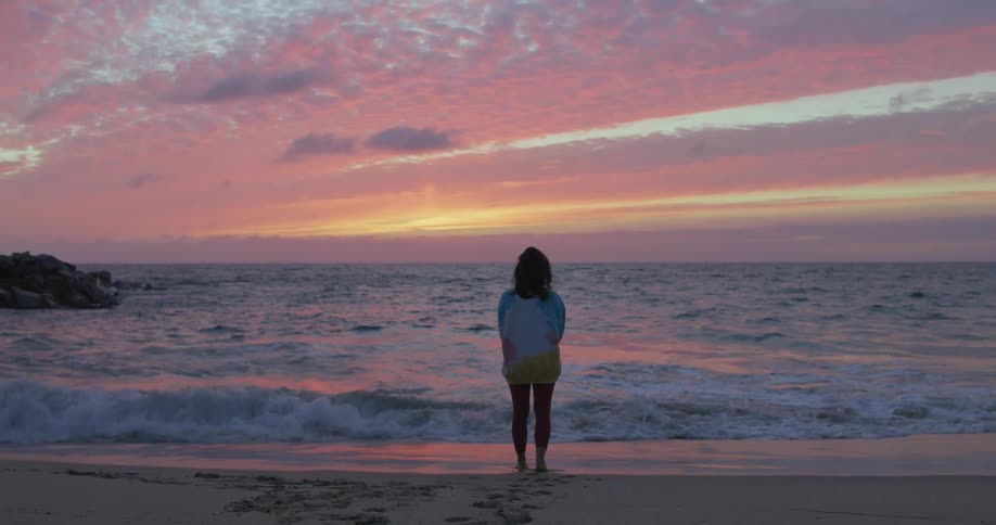 A woman is walking on the beach at dusk