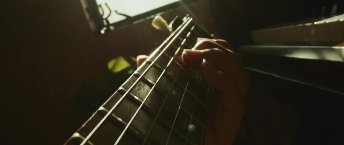 A person playing a guitar next to a piano with a plant and a window in the background