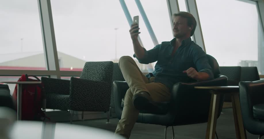 A man with a smart phone sitting on a chair in an airport