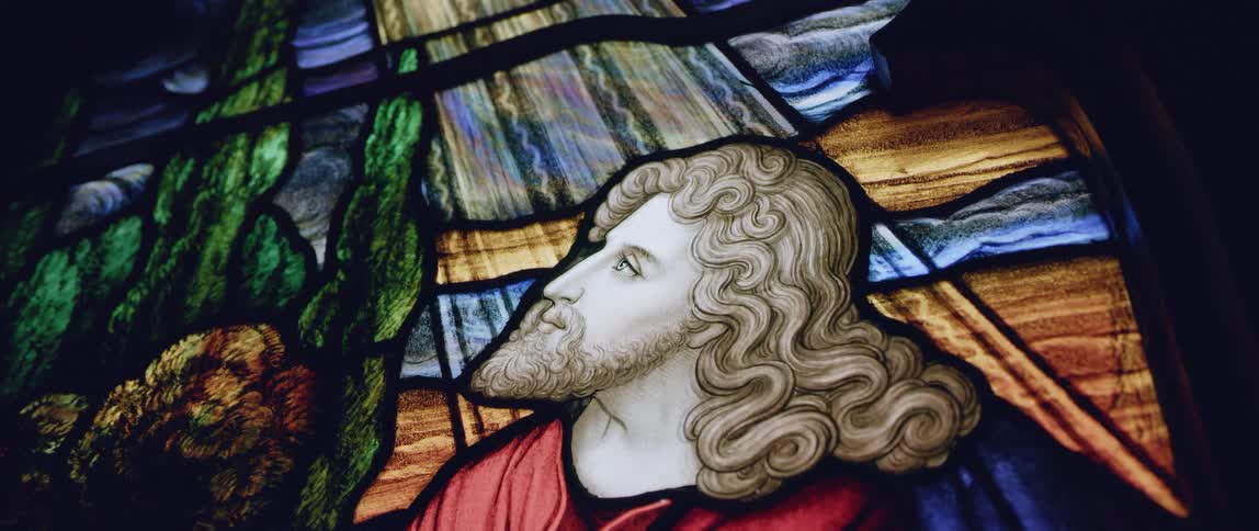 A close up of a stained glass window with a man with a beard and wavy hair