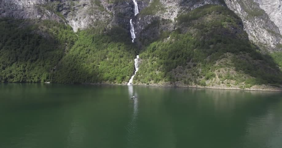 A waterfall falls down a steep hillside into a body of water with a boat in it