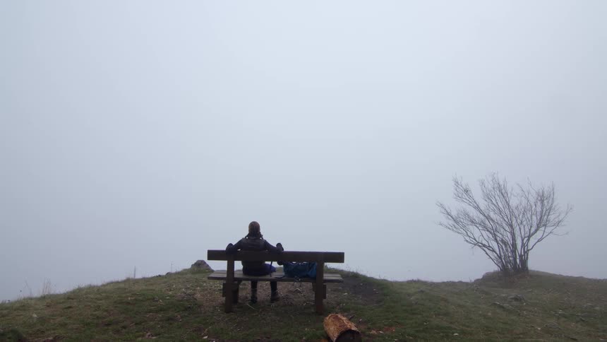 Young fit woman sitting on a bench in a hill looking at the fog covering the horizon