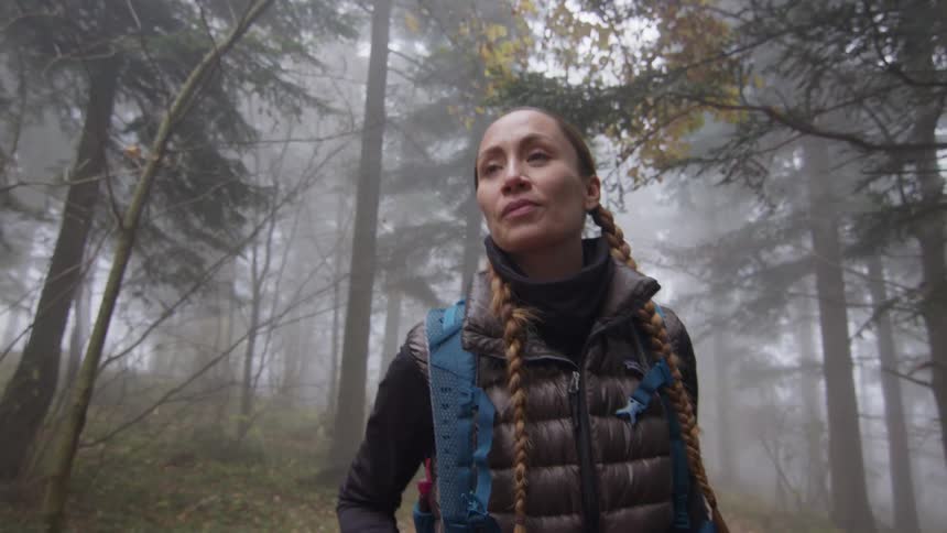 Young woman hiking on a trail throught the mist covered forest